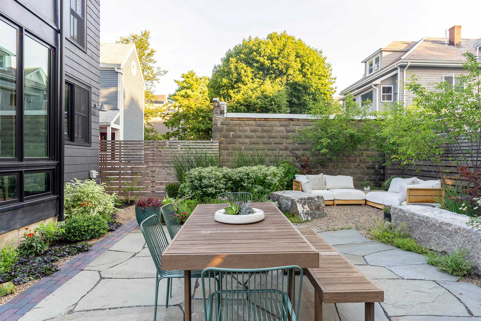 The dining terrace is positioned to connect directly to the home, with bluestone paving and layered plantings creating a cohesive and usable outdoor room.