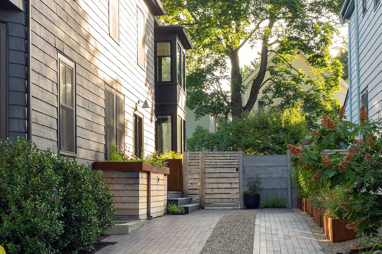 Permeable pavers with a central gravel band improve drainage while reinforcing the linear geometry of this narrow urban driveway, complemented by layered privacy screening.