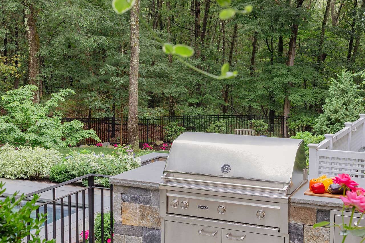 A built-in outdoor kitchen overlooks the pool and garden, integrating cooking, circulation, and landscape views into a single outdoor living zone, copyright: Michael J Lee