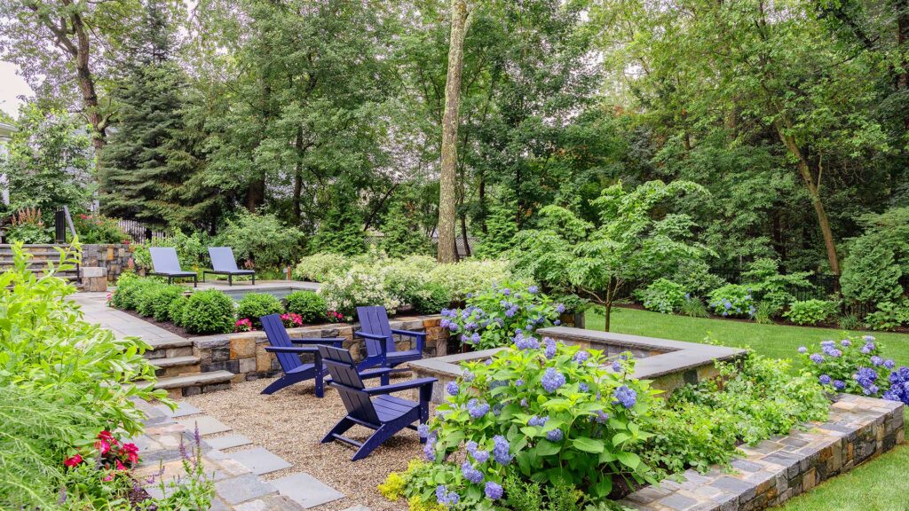 This gravel fire pit terrace is softened by hydrangeas and layered planting, offering a relaxed gathering space set slightly apart from the pool. photo credit: Michael J Lee