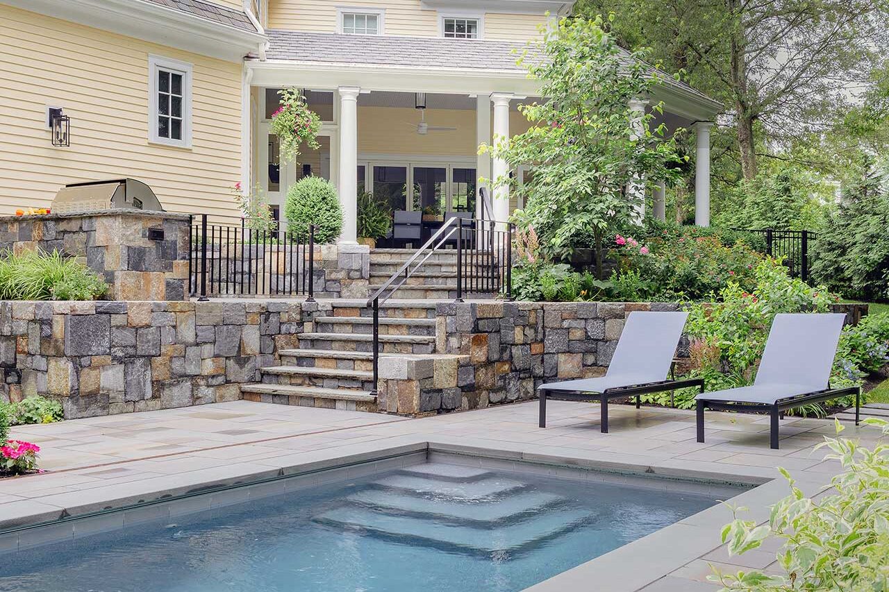 A compact pool, terraced stone walls, and a screened porch work together to create a cohesive outdoor living landscape on a challenging sloped site, copyright: Michael J Lee