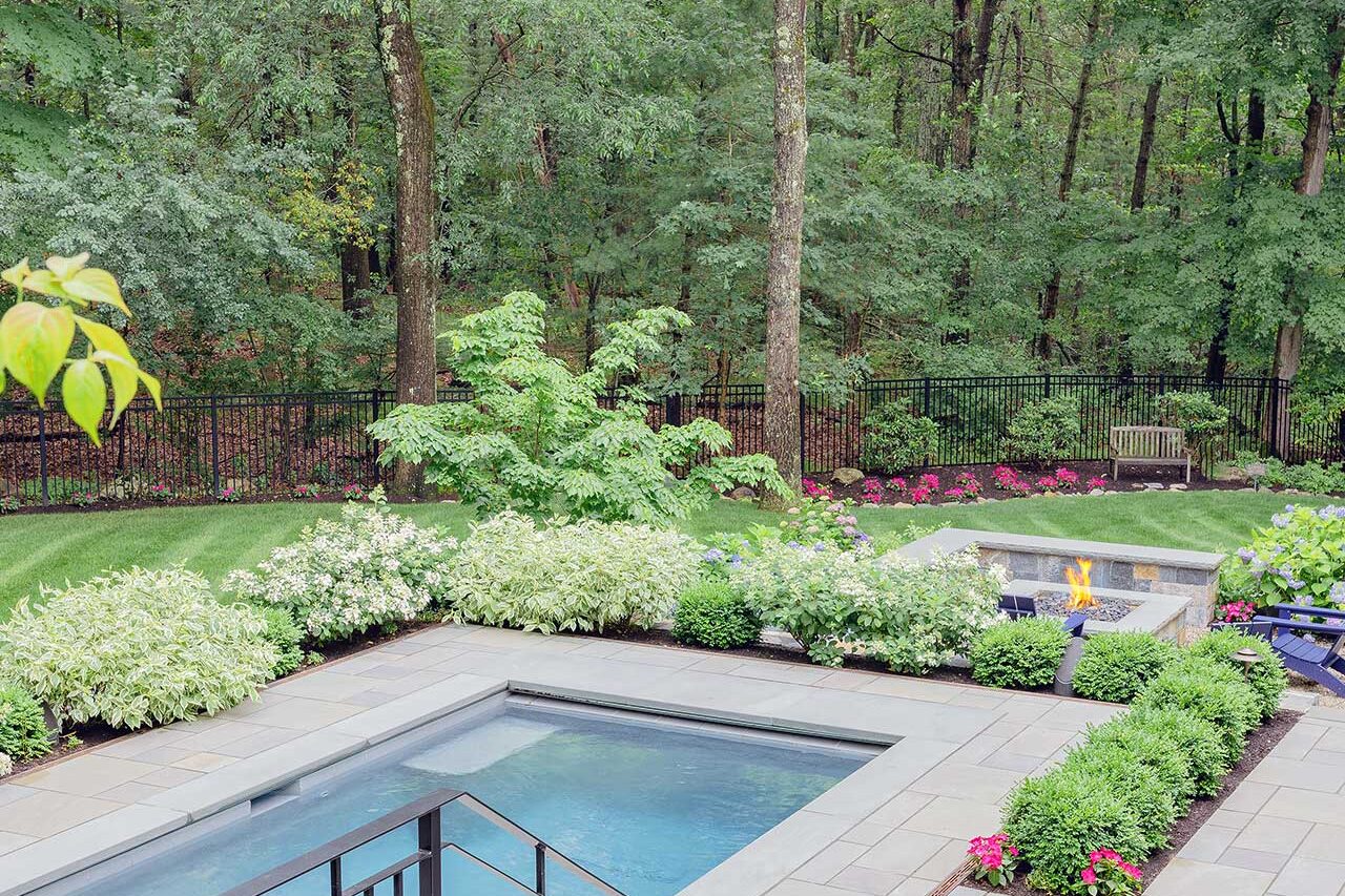 The pool terrace and fire feature are set within layered planting beds and backed by mature trees, giving the landscape a private, resort-like feel, copyright: Michael J Lee