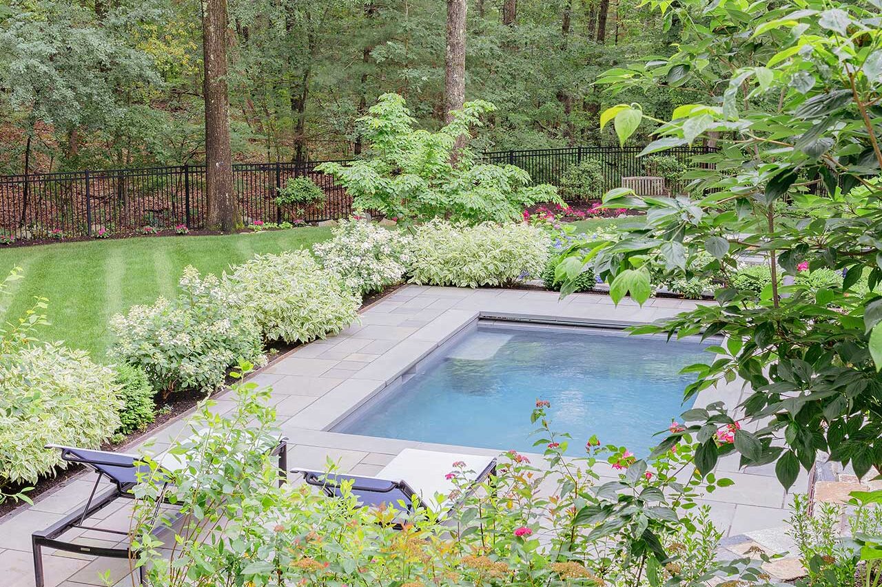 The pool terrace sits comfortably within a framework of flowering shrubs, clipped evergreens, and mature woodland, balancing openness with privacy, copyright: Michael J Lee