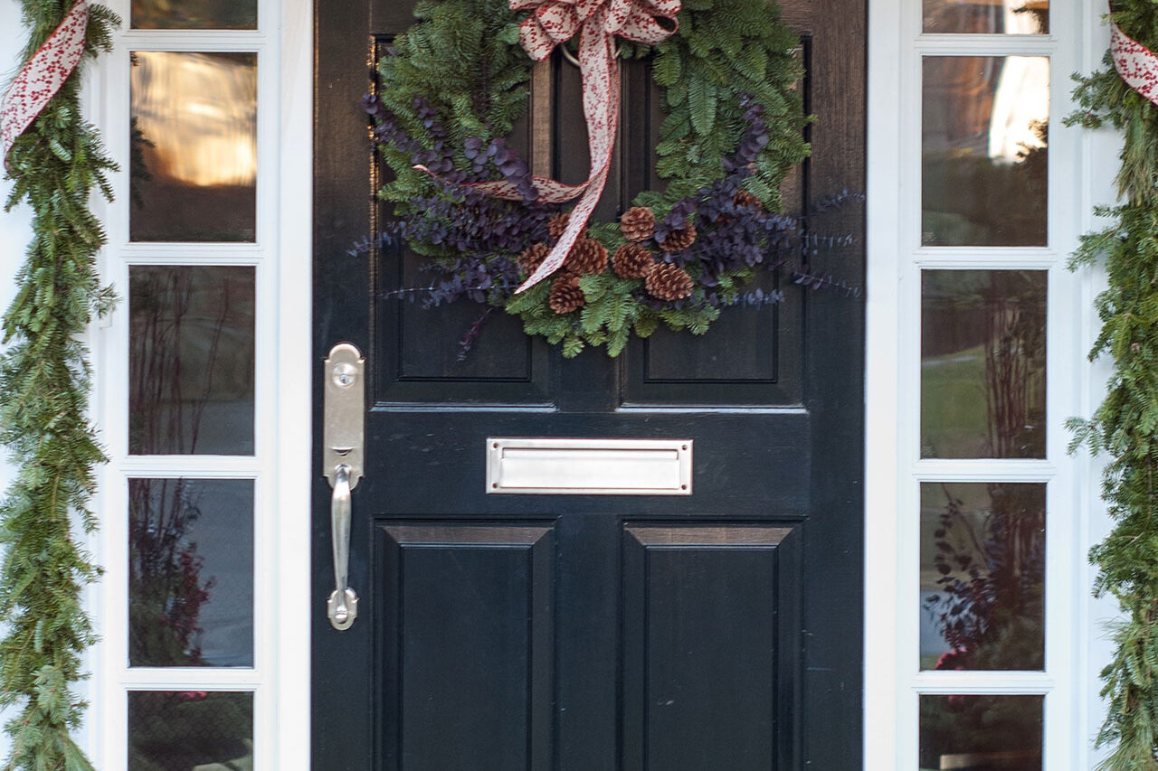 Wreath and garland work together to frame the door, creating a cohesive holiday look rooted in New England tradition.