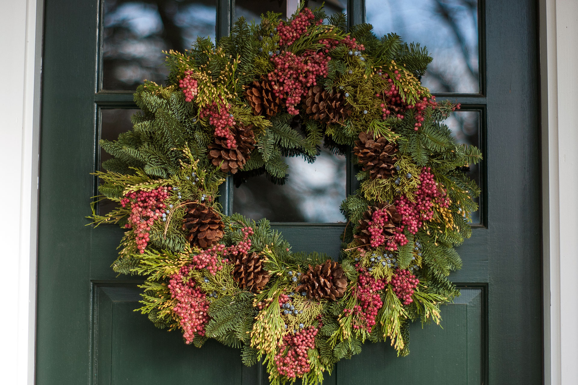 Fresh evergreen wreath with winter berries adds natural color and understated holiday charm, complementing classic New England entry doors.