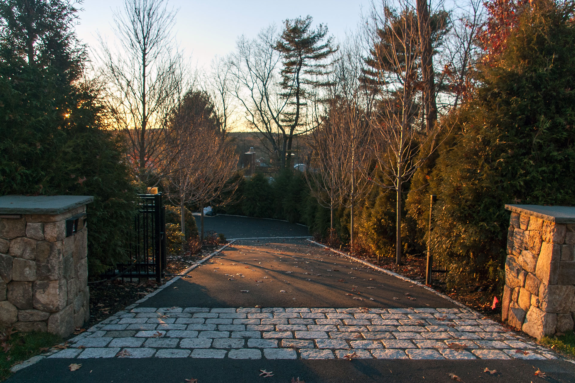 This asphalt driveway is anchored by stone gate posts and warm evening light, delivering a reliable surface with visual interest during autumn arrivals.
