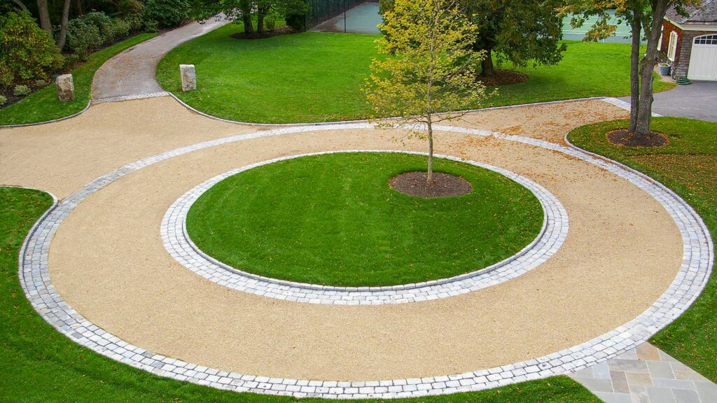 This circular gravel driveway features a cobblestone ring and planted center island, organizing traffic flow while adding visual focus and texture.