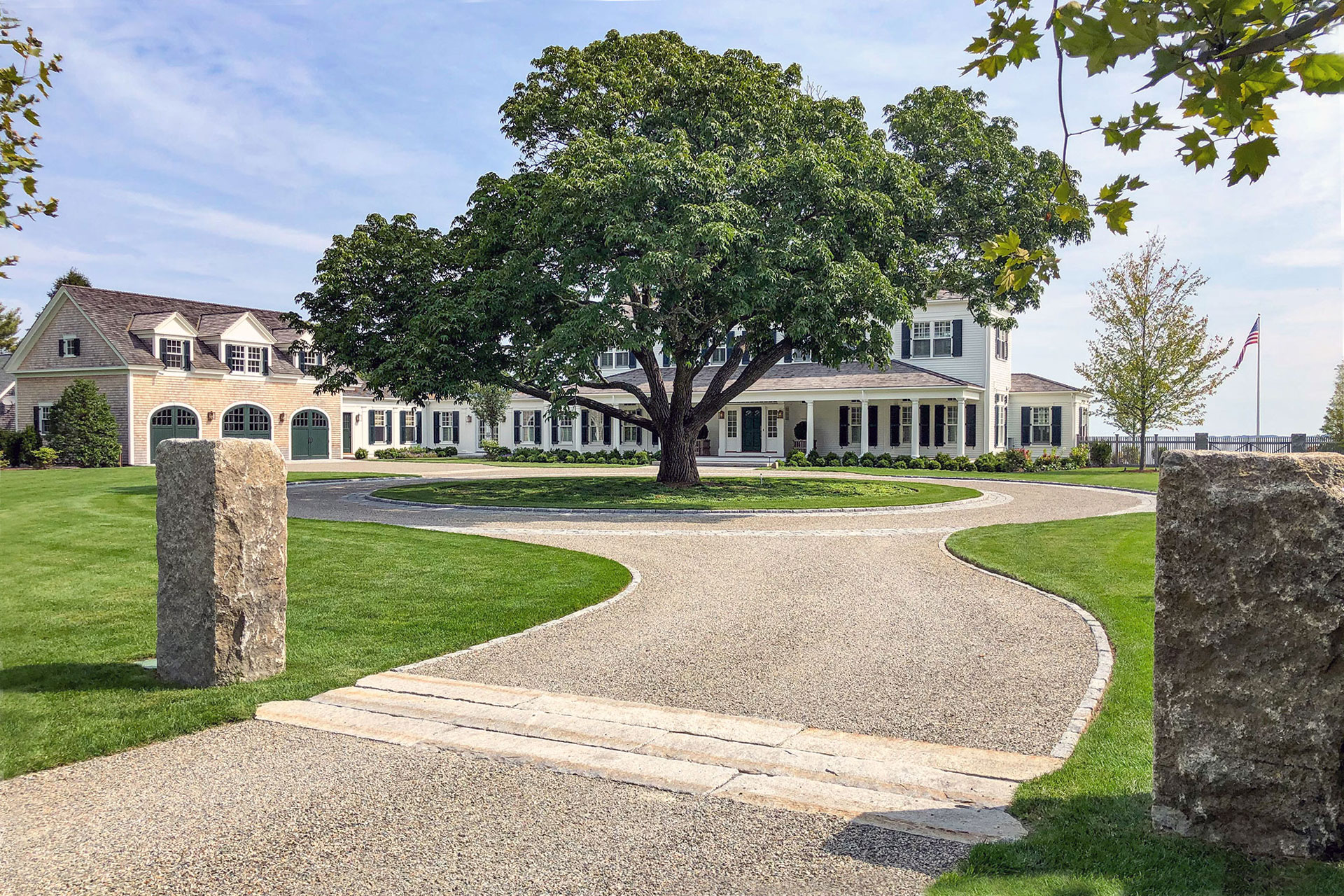 A formal circular gravel driveway anchors a grand estate entry, framed by stone pillars that add structure, durability, and a strong sense of arrival without feeling overly rigid.