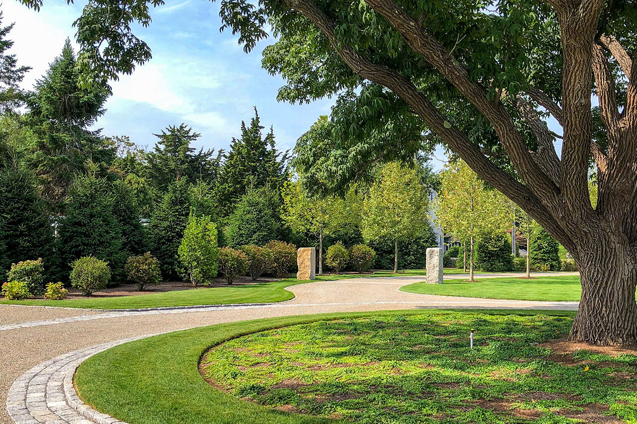 A curved gravel driveway lined with evergreen borders creates year-round structure, guiding visitors toward the estate with consistent color and form.
