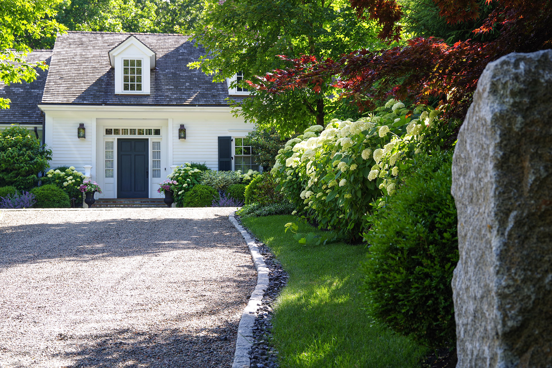 In Weston, MA, granite edging frames a curved gravel driveway beneath mature trees, preserving roots while maintaining clean lines and controlled edges.