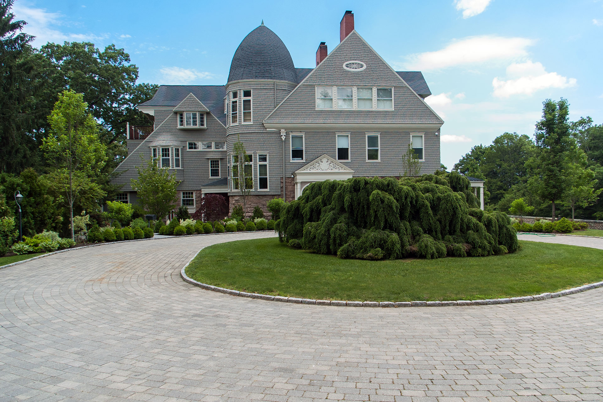 A curved gravel driveway runs alongside a stone wall and flowering trees, creating a seasonal spring approach that feels established and inviting.