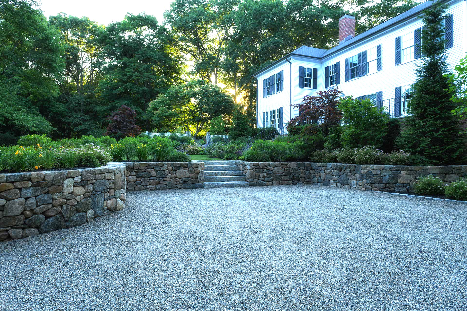This formal gravel court is supported by stone retaining walls, organizing circulation and grade changes while reinforcing the stately character of a colonial estate.