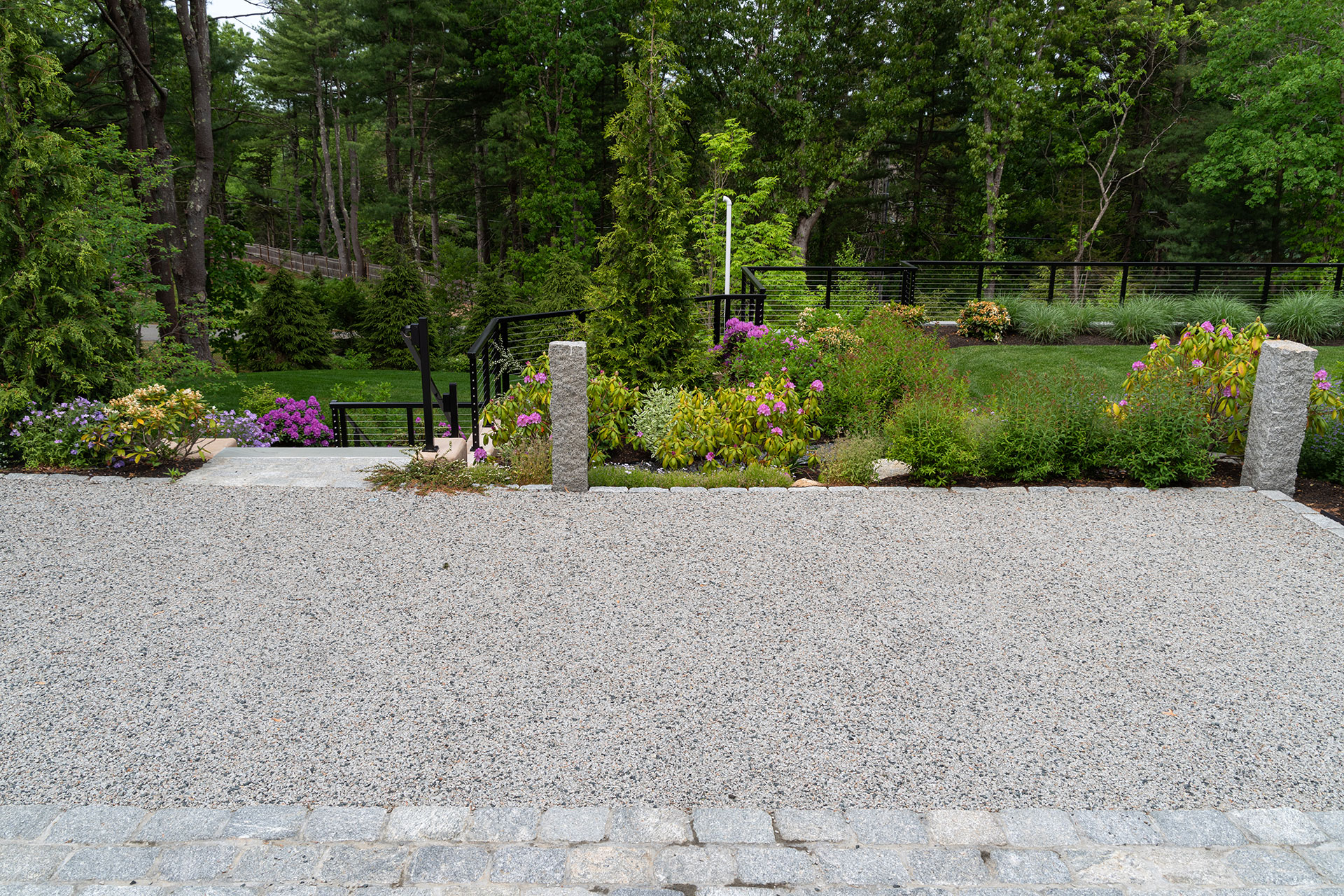Granite curbing defines this gravel driveway, working with modern railings and terraced grades to manage elevation changes and create a cohesive, structured look.