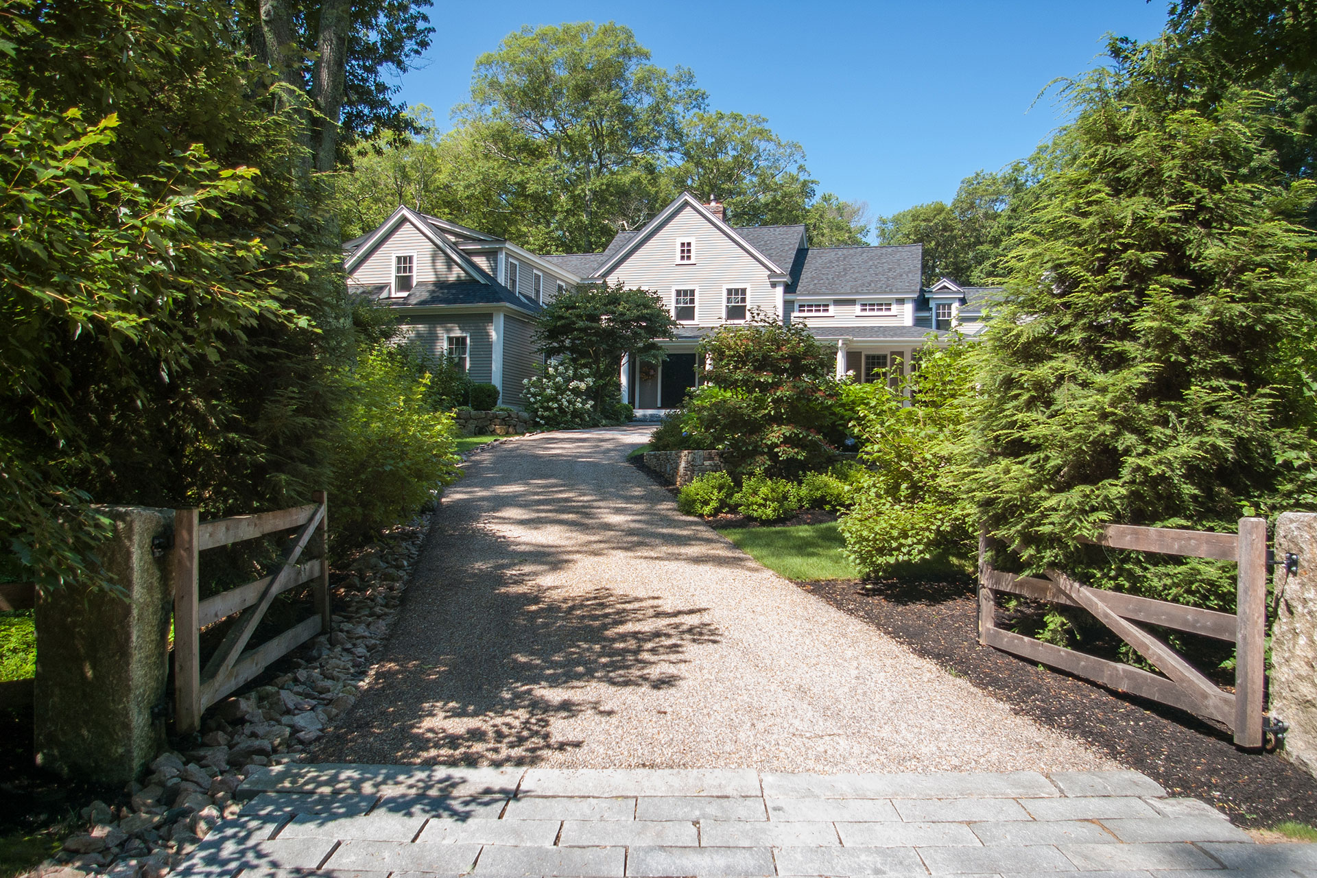 A gravel driveway framed by wood gates transitions seamlessly into a naturalistic landscape, offering durability and drainage while maintaining an understated arrival sequence.