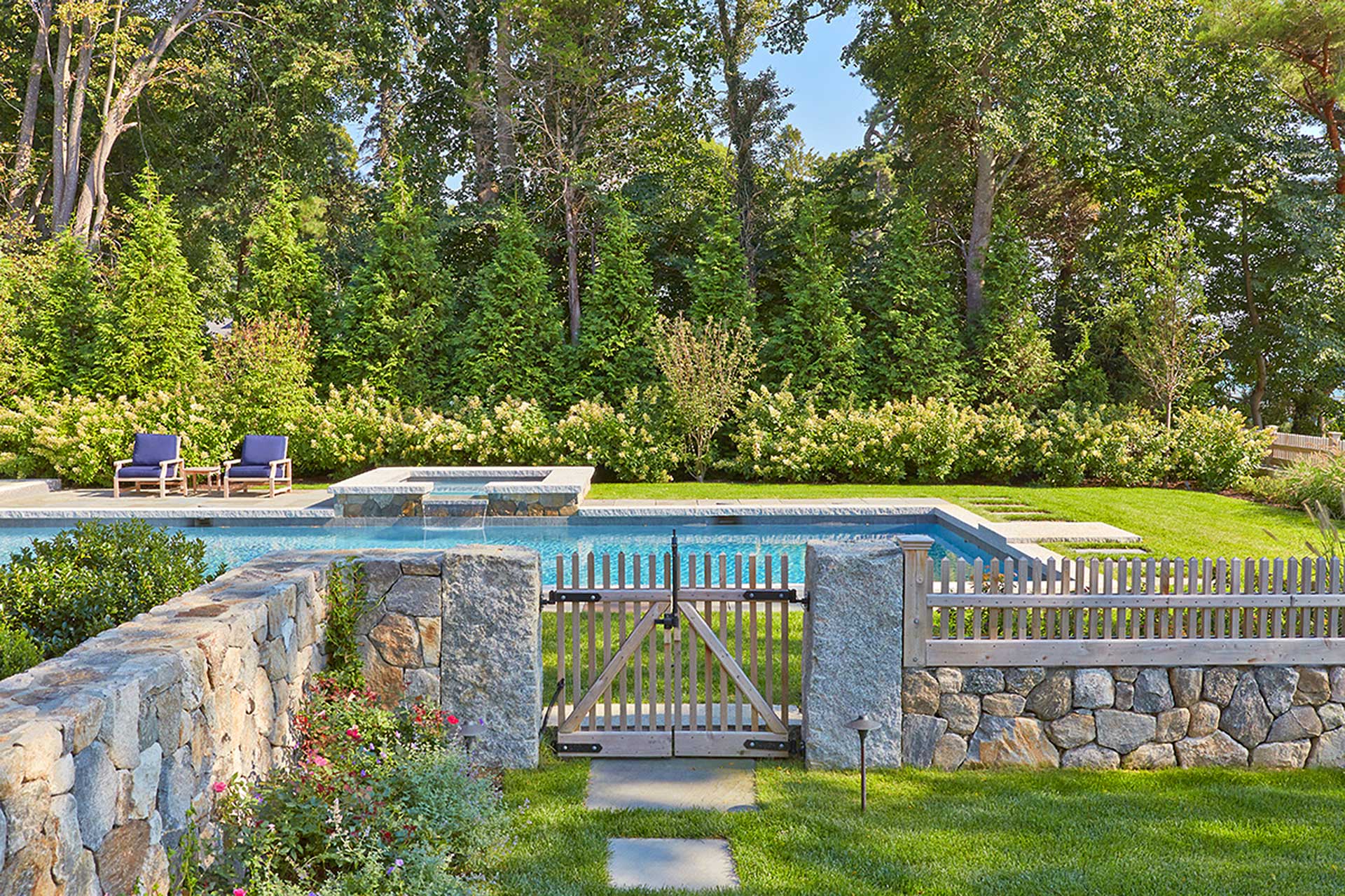 Evergreen screening, flowering shrubs, and mature trees create privacy around pool.