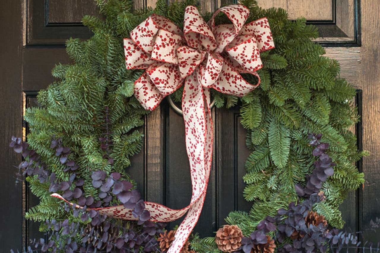 A full evergreen wreath layered with eucalyptus, pinecones, and patterned ribbon gives the entry a refined holiday finish.