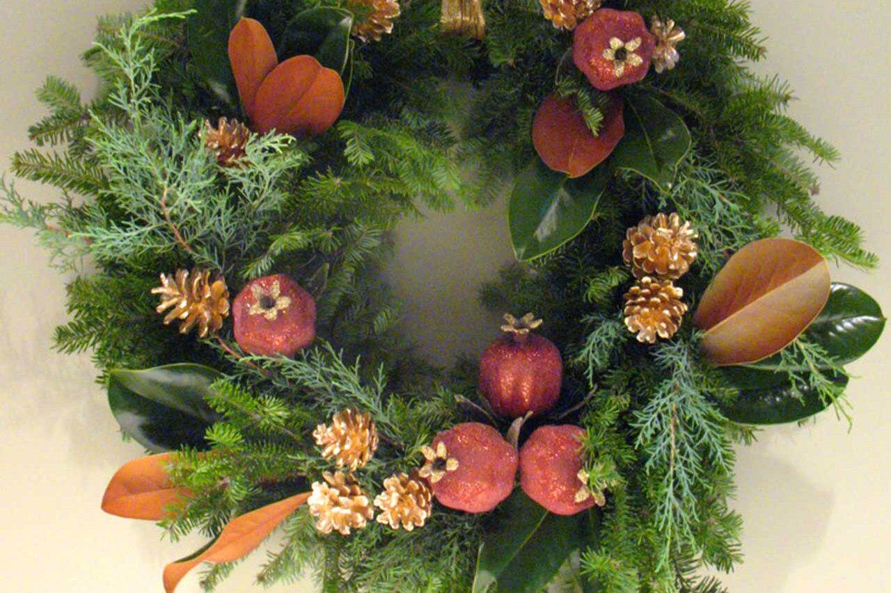 A richly layered wreath with magnolia leaves, gold pinecones, and pomegranate accents brings warm, natural elegance to the entry.