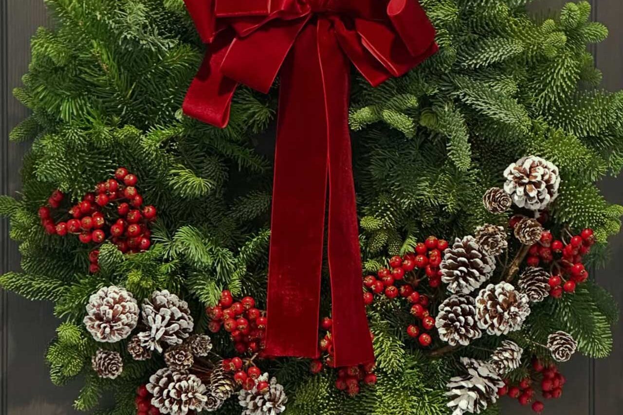 With its red velvet bow, berries, and frosted pinecones, this wreath adds bold color and festive contrast to the dark door.