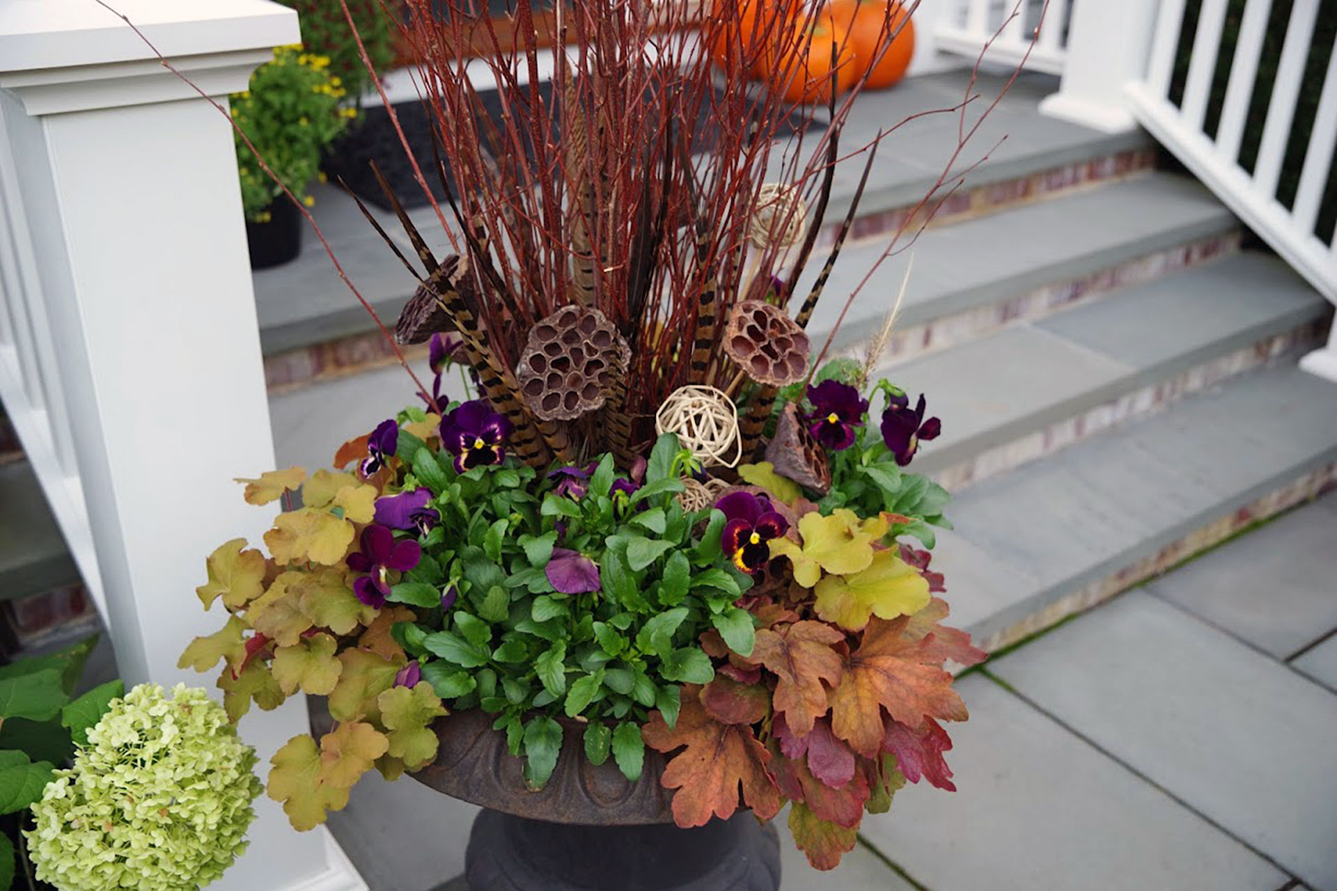 An autumn urn with branch accents, pansies, and textured foliage softens front steps, demonstrating how fall containers guide movement and add charm.
