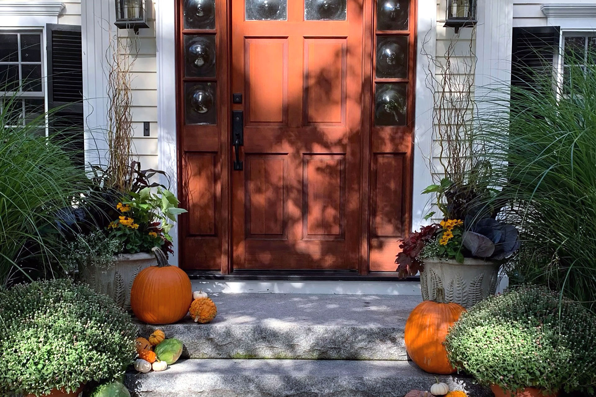 Brookline, MA colonial entry styled with pumpkins, planters, and fall florals balances tradition and color, enhancing curb appeal through seasonal accents.