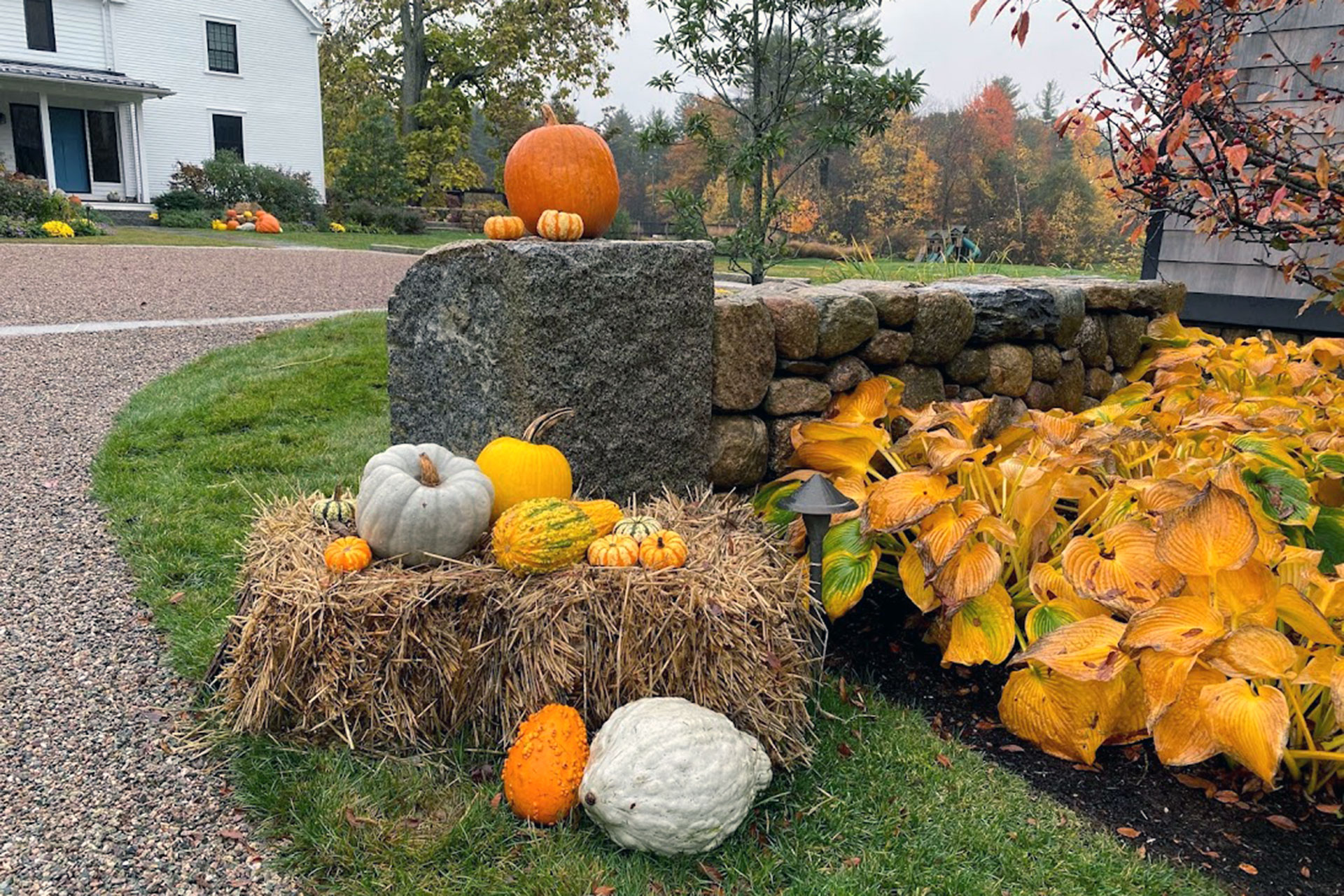 A fieldstone wall edge highlighted with pumpkins adds subtle seasonal interest along the driveway, proving fall decor can be understated yet impactful.
