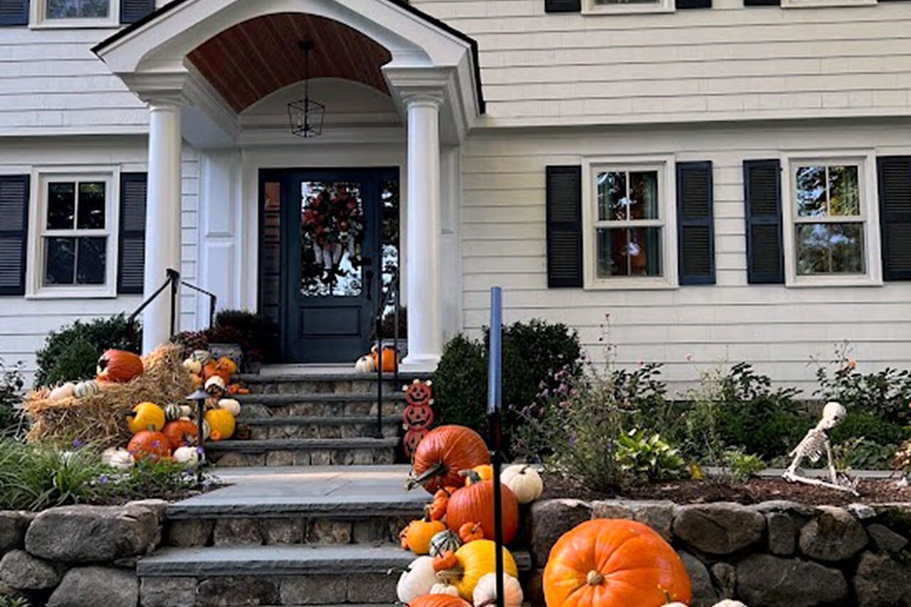 A formal front entry dressed with pumpkins and hay bales blends symmetry and fall color, showing how seasonal displays complement refined landscapes.