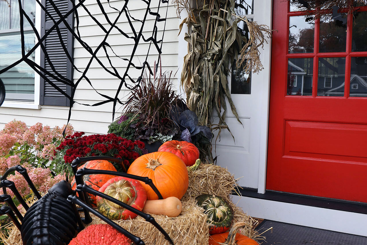 Front porch decor with spider webs, cornstalks, and pumpkins creates a festive harvest entry that can shift easily from fall elegance to Halloween fun.