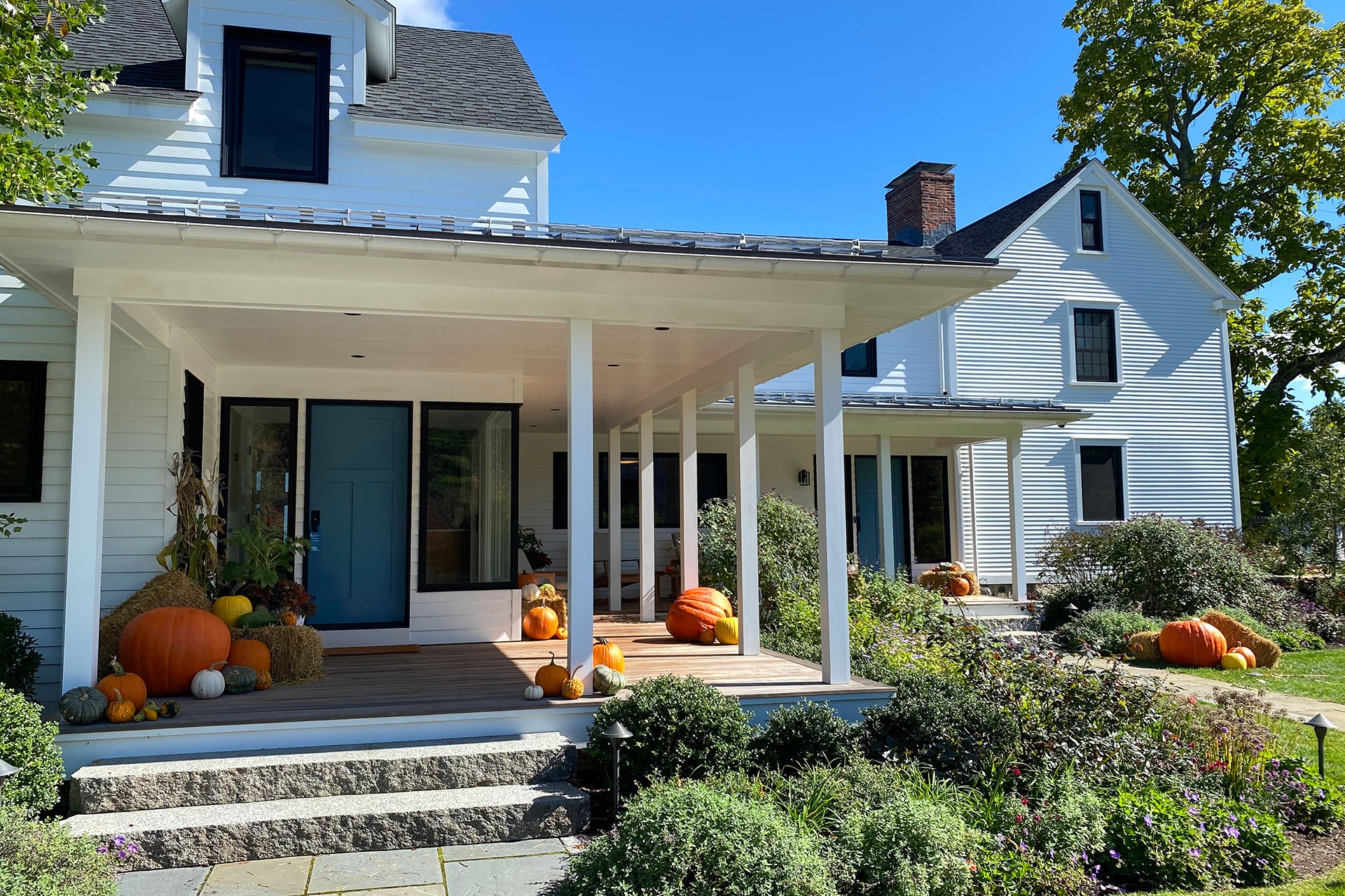 A modern farmhouse porch styled with pumpkins and hay bales creates a warm, welcoming entry, blending rustic materials with playful fall flair and plenty of design flexibility.