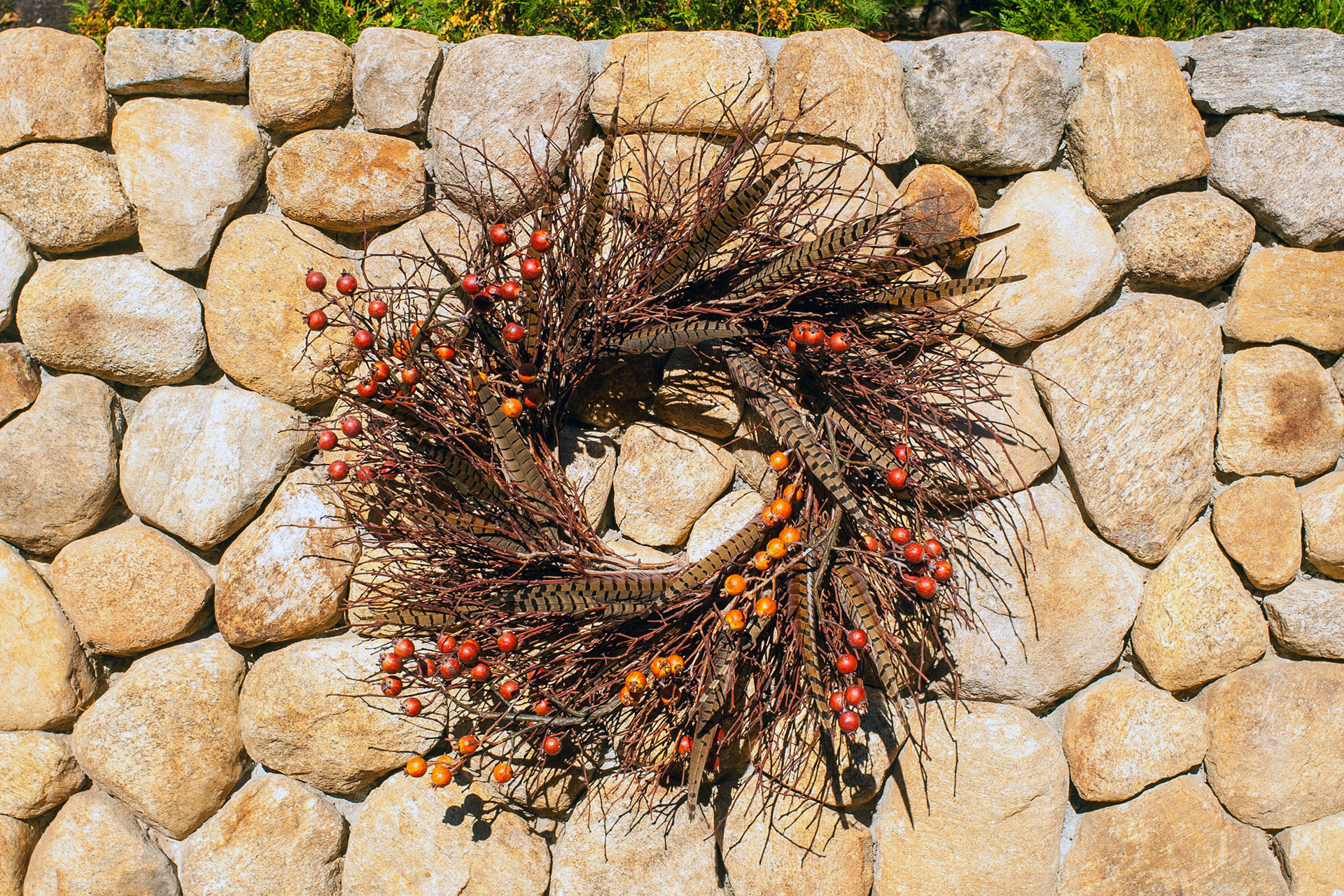 A branch wreath with orange berries mounted on a fieldstone wall offers a natural fall accent, adding seasonal texture without overwhelming the space.