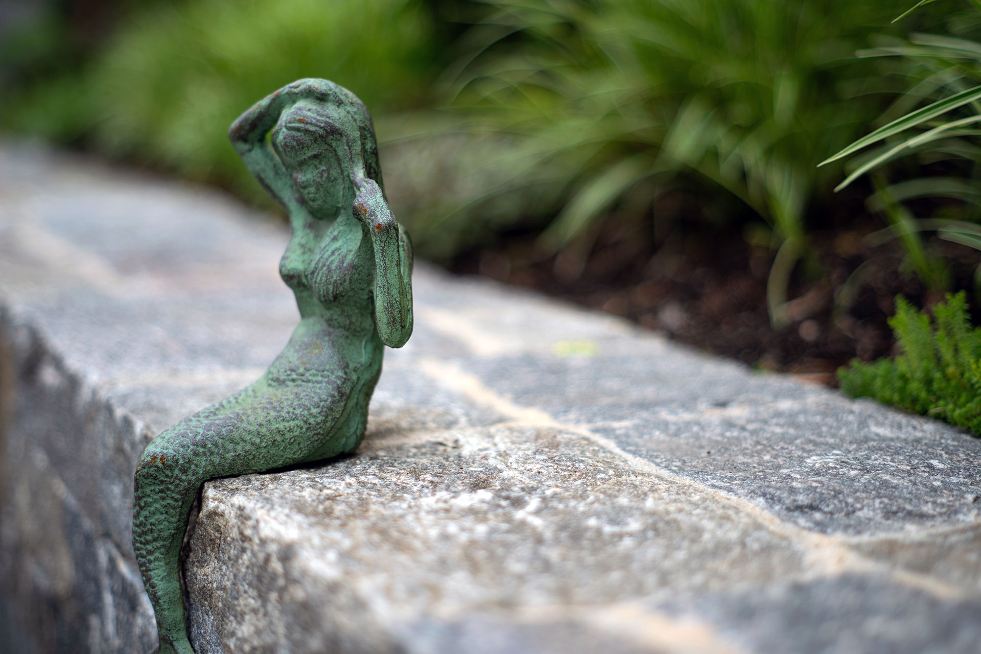 A bronze figurative sculpture mounted along a stone wall adds depth and artistry, using shadow, texture, and patina to enrich the garden edge.