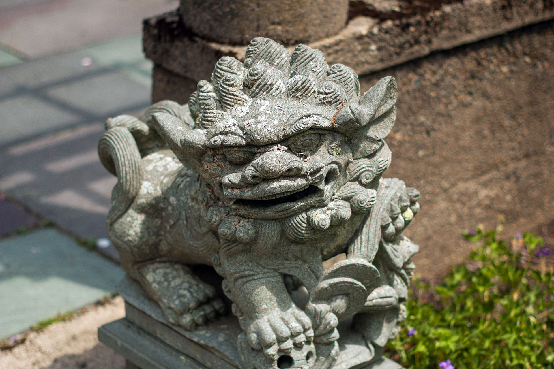 A carved stone foo dog guardian sculpture flanks the entryway, offering bold presence and historic character that signals arrival and anchors the landscape.