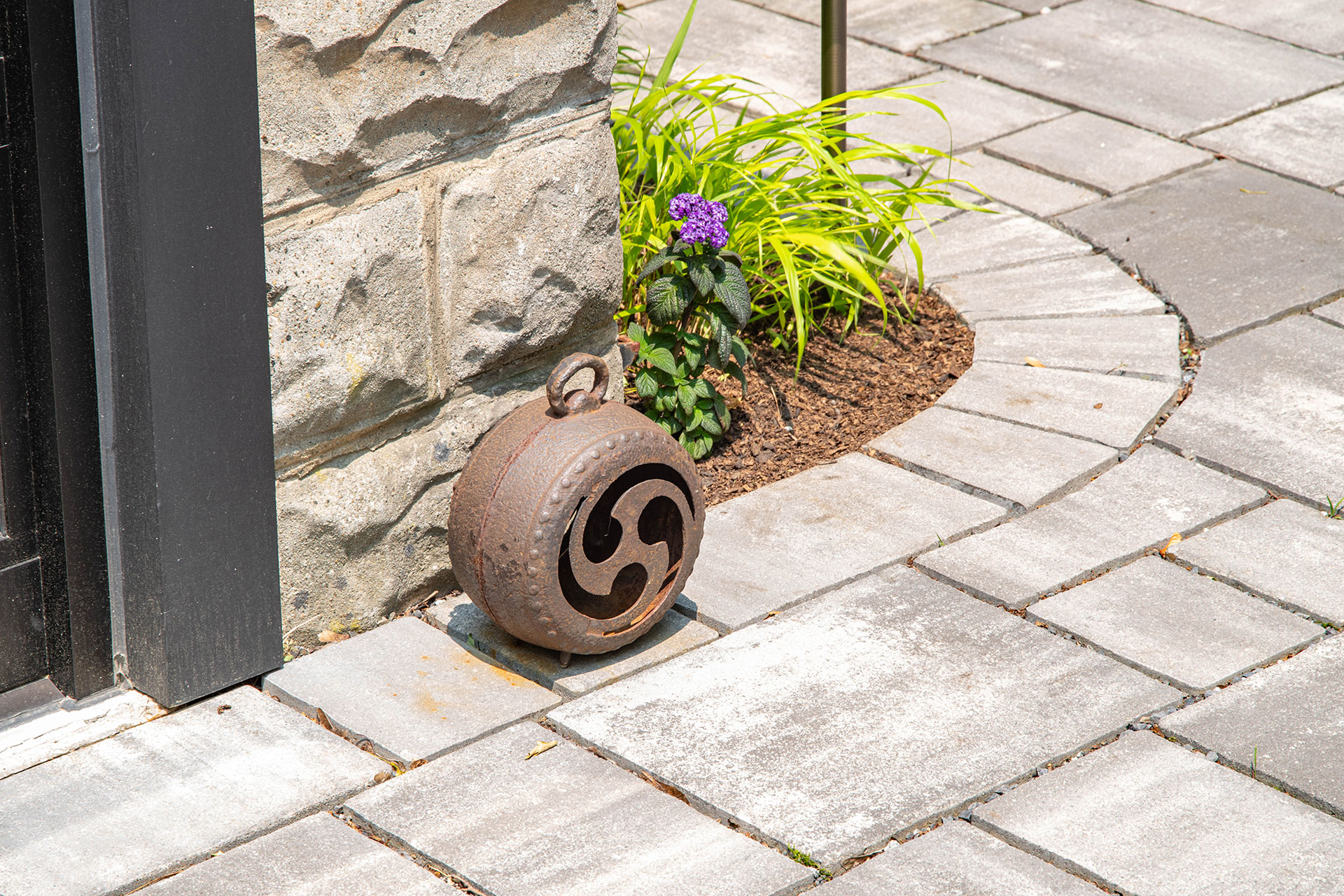 This cast iron lantern accent sits along a stone paver walkway, adding old-world charm and visual weight while complementing traditional hardscape materials.