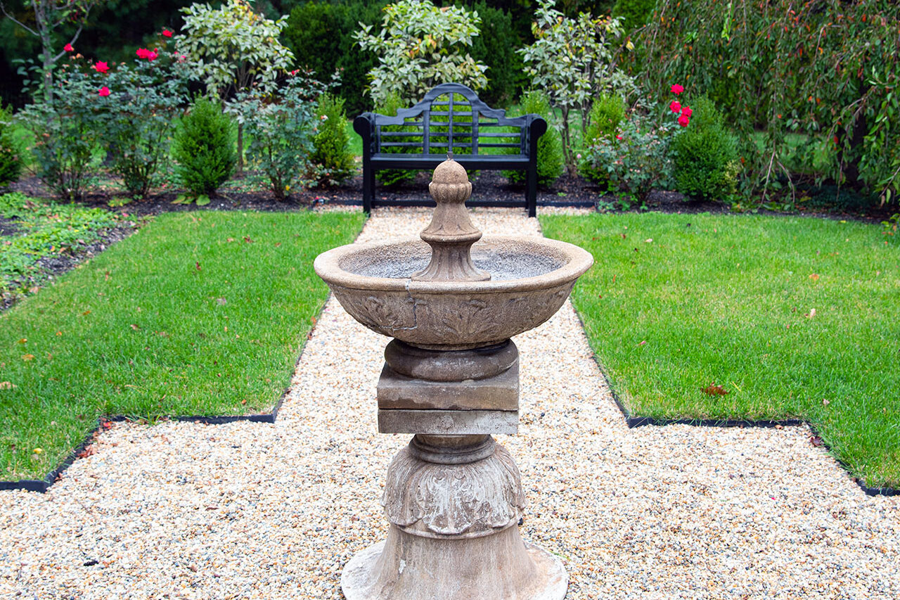 A tiered stone fountain forms the centerpiece of a symmetrical garden, offering soothing movement, balanced proportions, and a strong sense of traditional elegance.