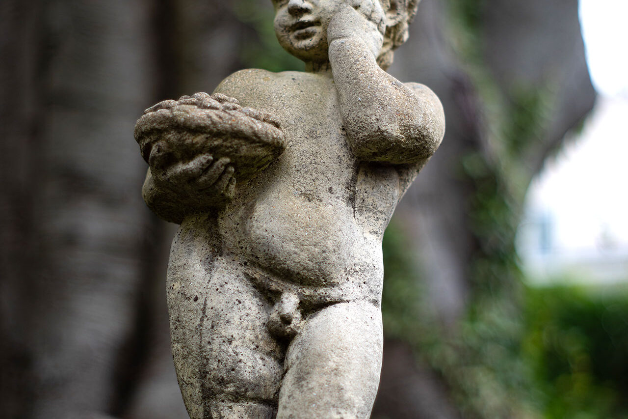 This classical stone cherub statue in Lincoln, MA rests within a woodland garden, its soft form and aged finish enhancing the tranquil, secluded atmosphere.