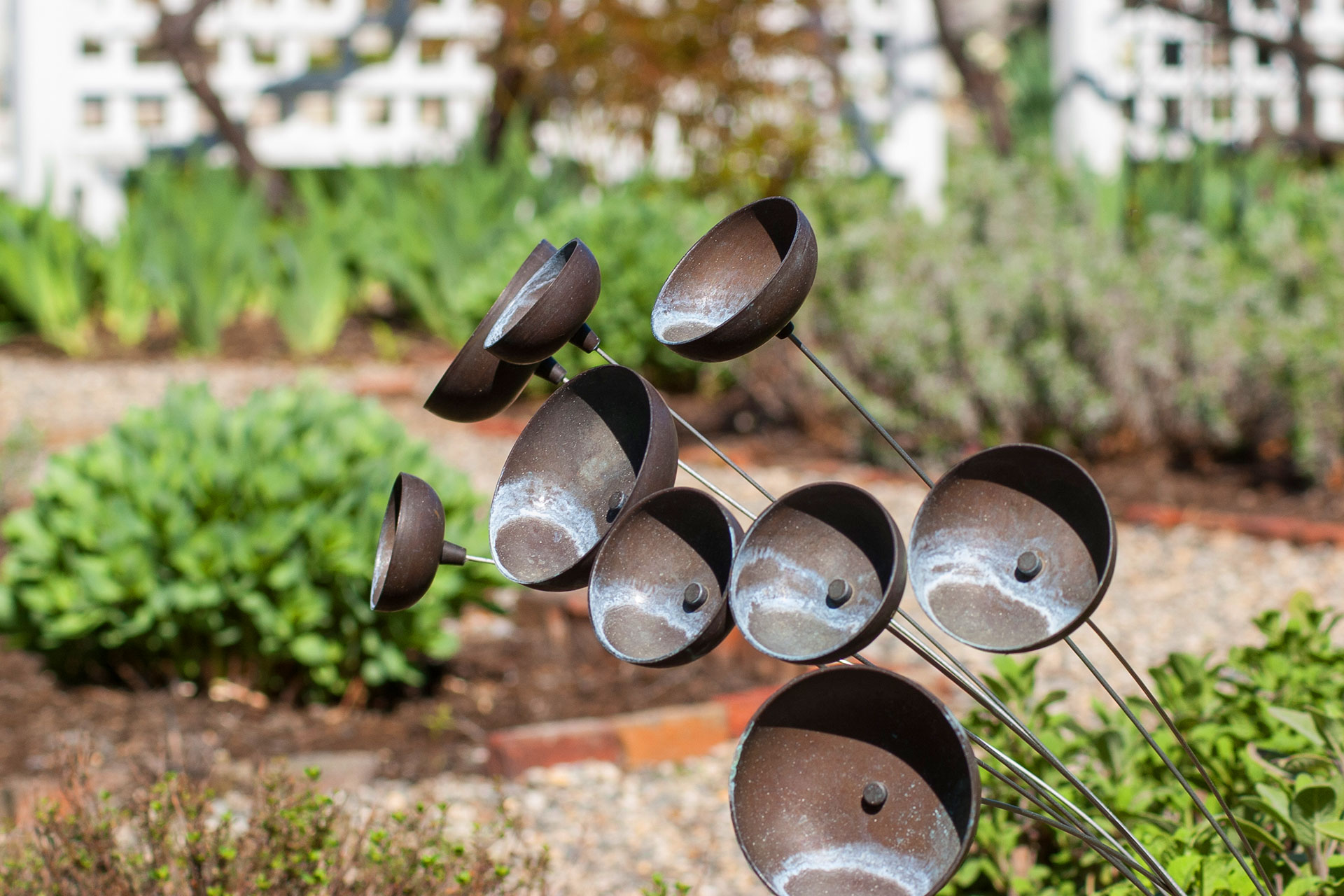 This modern abstract metal garden sculpture adds contrast to lush planting beds, using clean lines and dark tones to create a contemporary focal point within soft greenery.