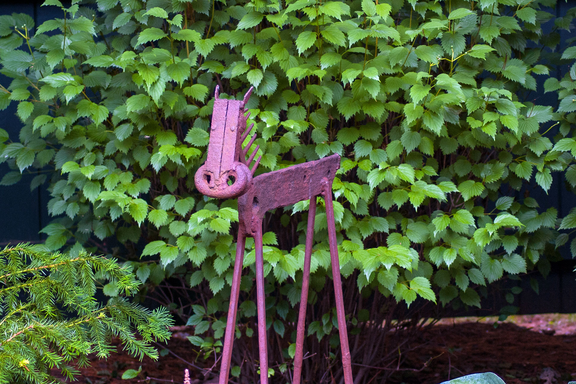 A rustic steel animal sculpture tucked into a shade garden in Lincoln, MA adds character and surprise, its weathered finish echoing bark, leaf litter, and natural tones.