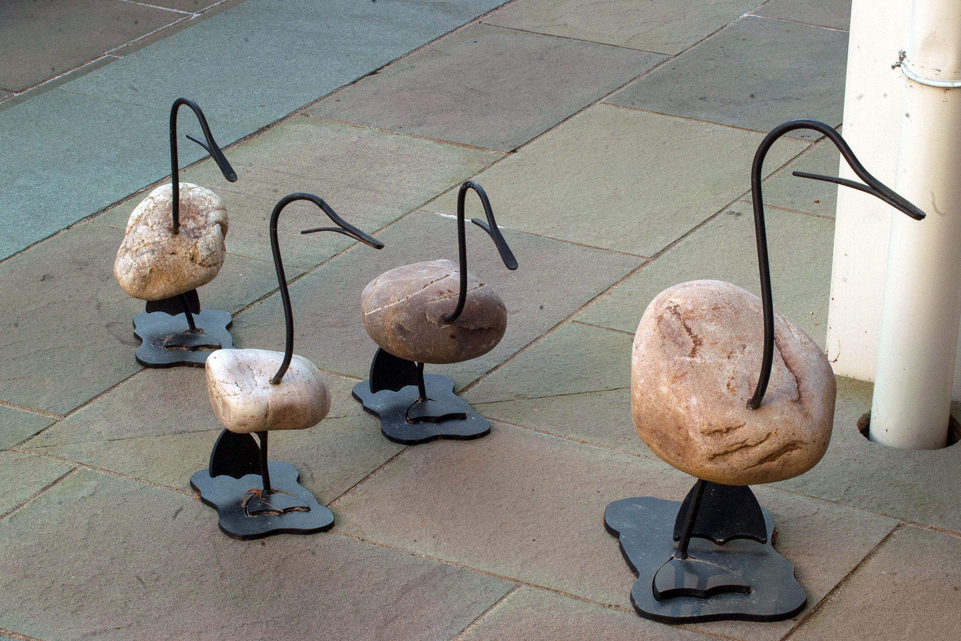 Whimsical stone bird sculptures with metal legs add playful movement to this Wellesley, MA patio display, blending sculptural art with casual outdoor living spaces.