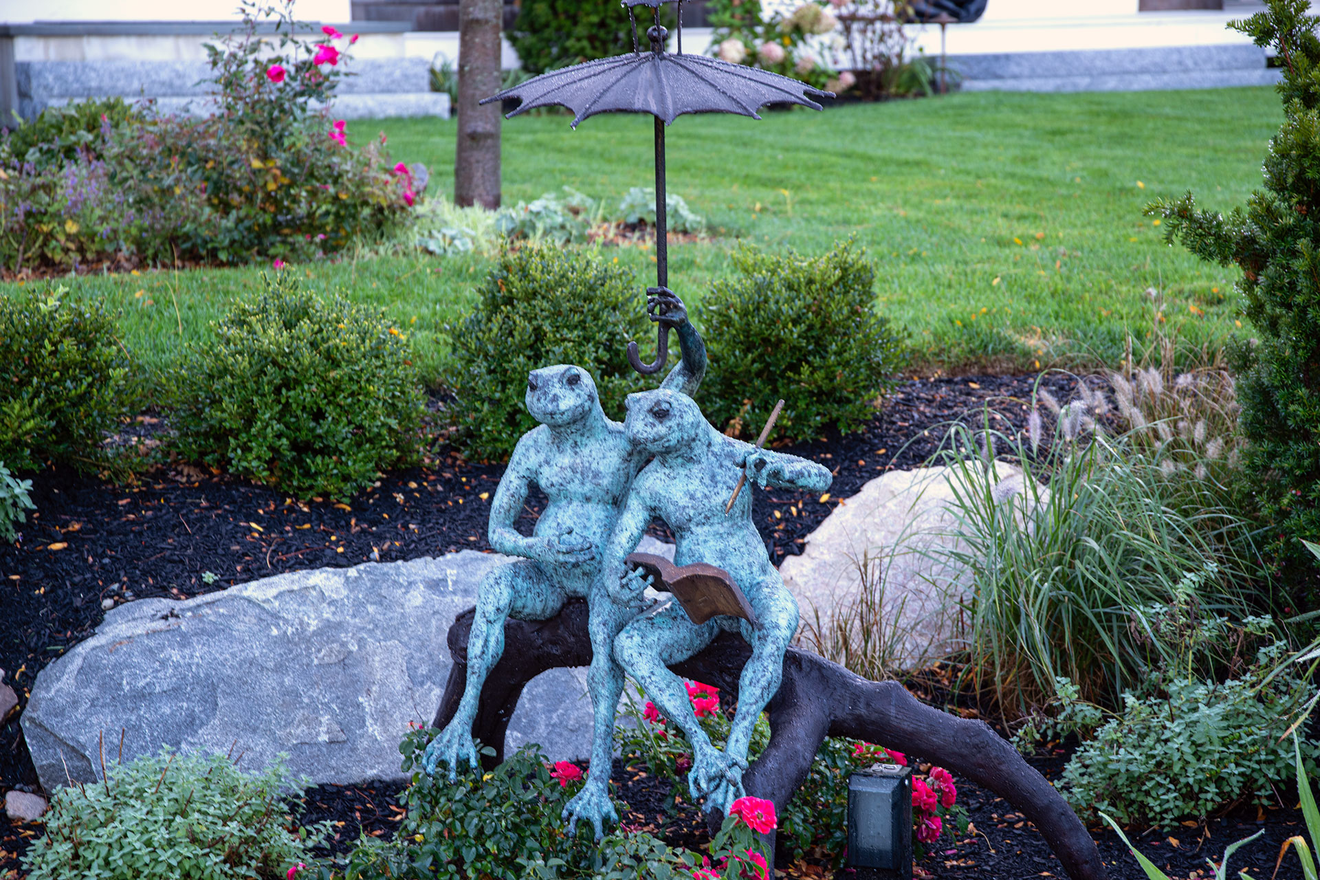 A whimsical bronze frog sculpture with a soft green patina adds charm and personality to a shaded reading garden, offering playful contrast against layered plantings and natural textures.