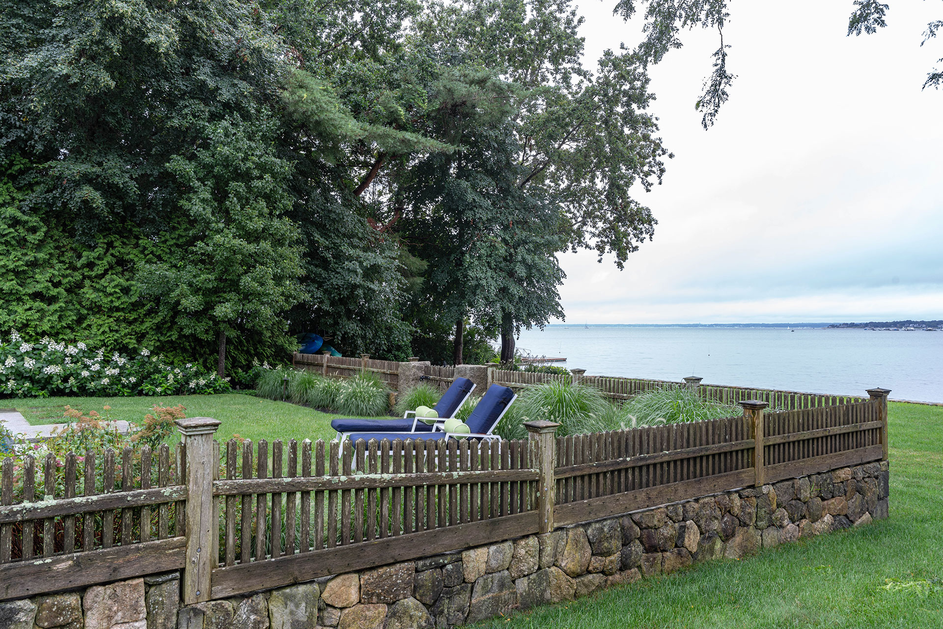 A coastal wood picket fence complements stone walls in Manchester-by-the-Sea, defining space without blocking ocean breezes.