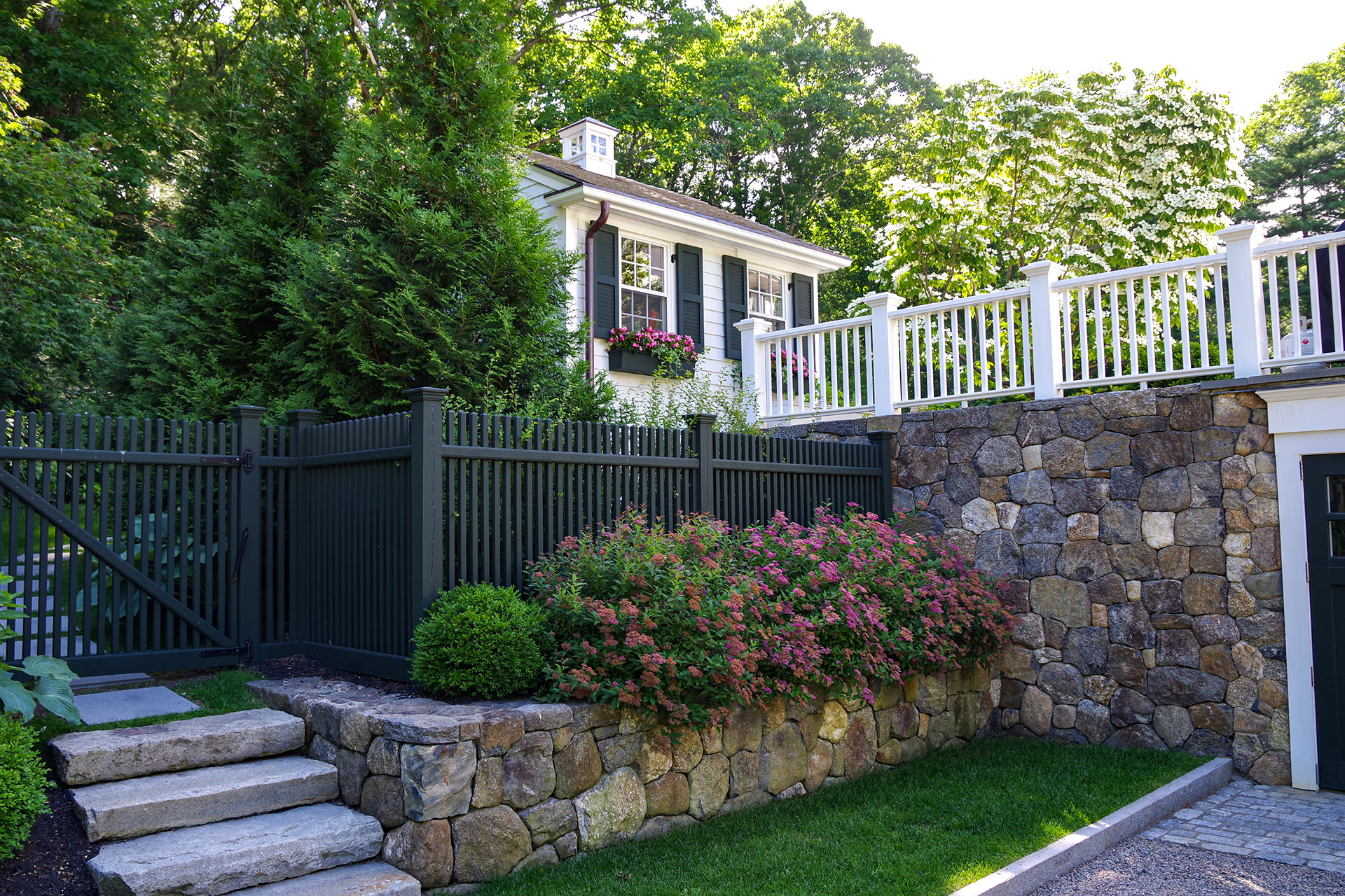 Layered fencing atop a stone wall addresses elevation changes, reinforcing privacy and safety while keeping the landscape organized.