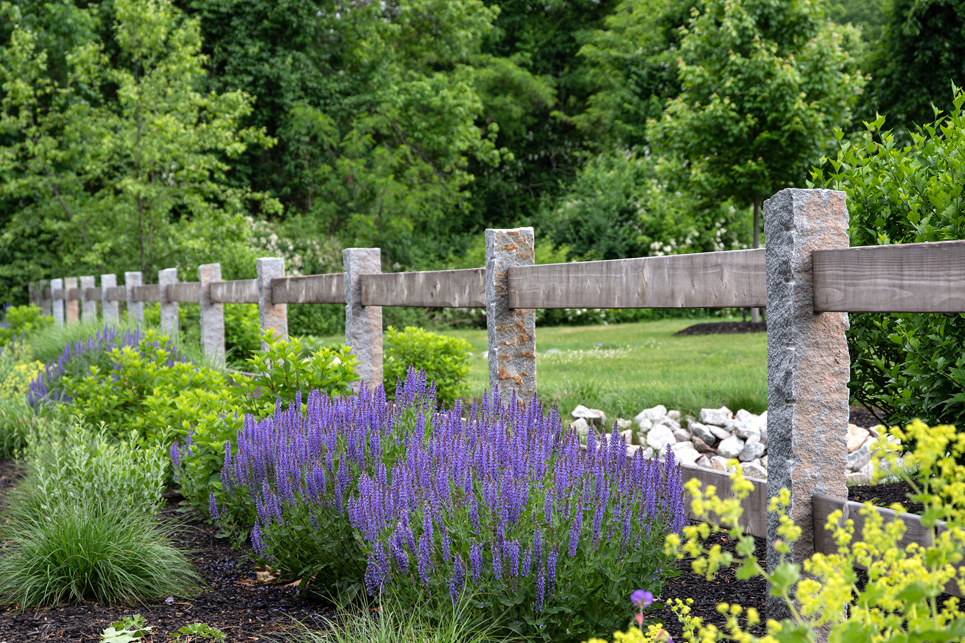 Wood rail fencing set between granite posts complements perennial gardens in Lexington with durability and classic appeal.