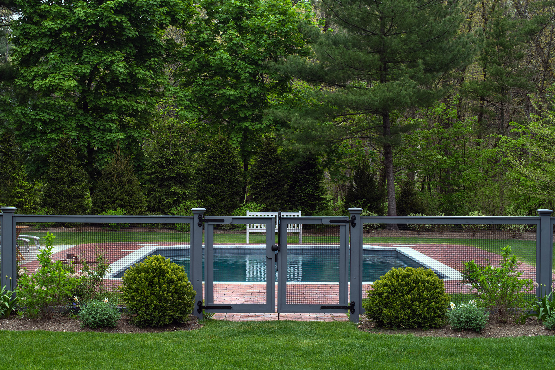 A discreet gray metal fence provides pool safety in a formal Weston backyard without disrupting the overall design.