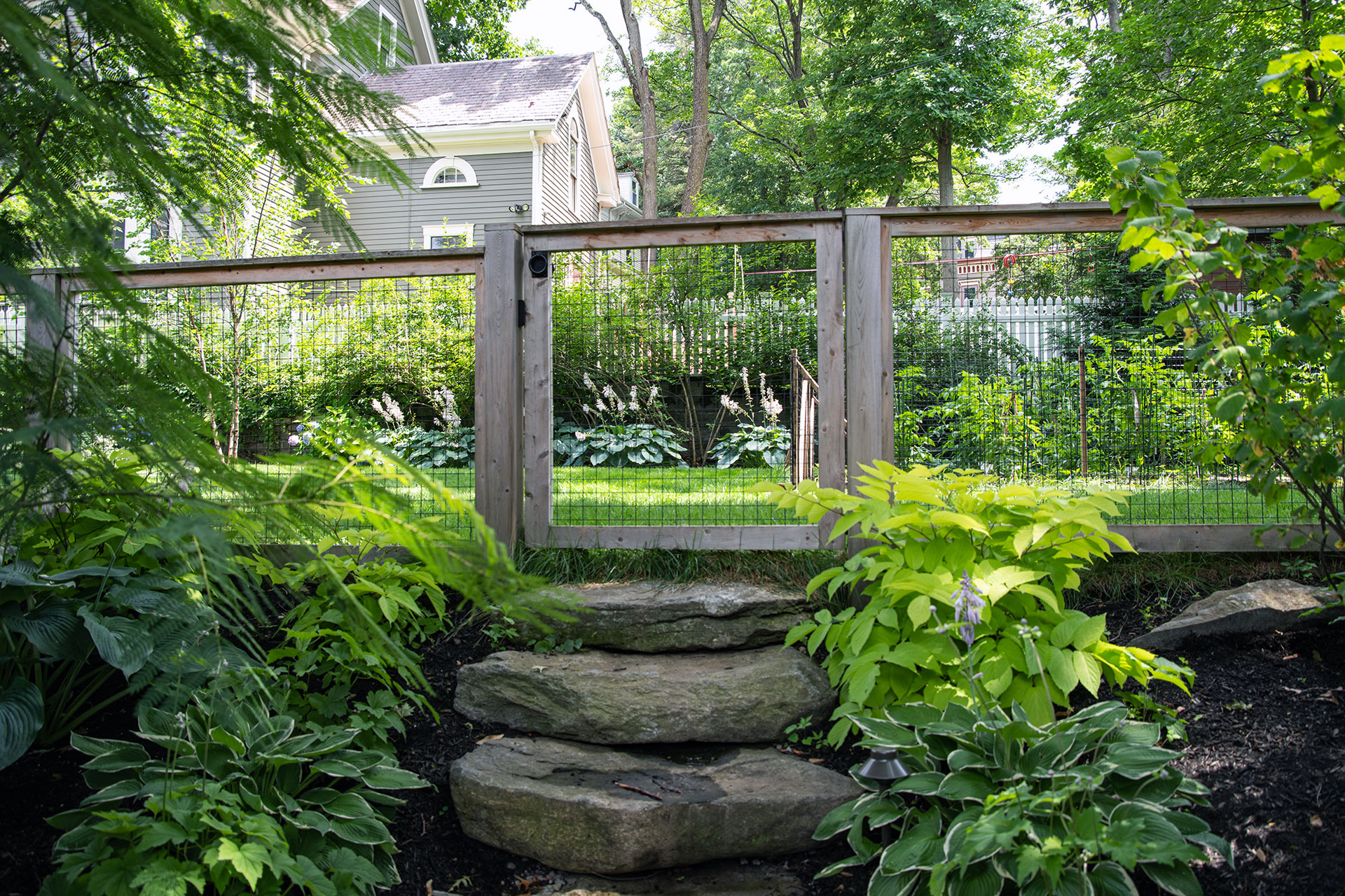This natural wood gate and fence guide movement through a shaded Brookline garden while blending seamlessly with stone steps.