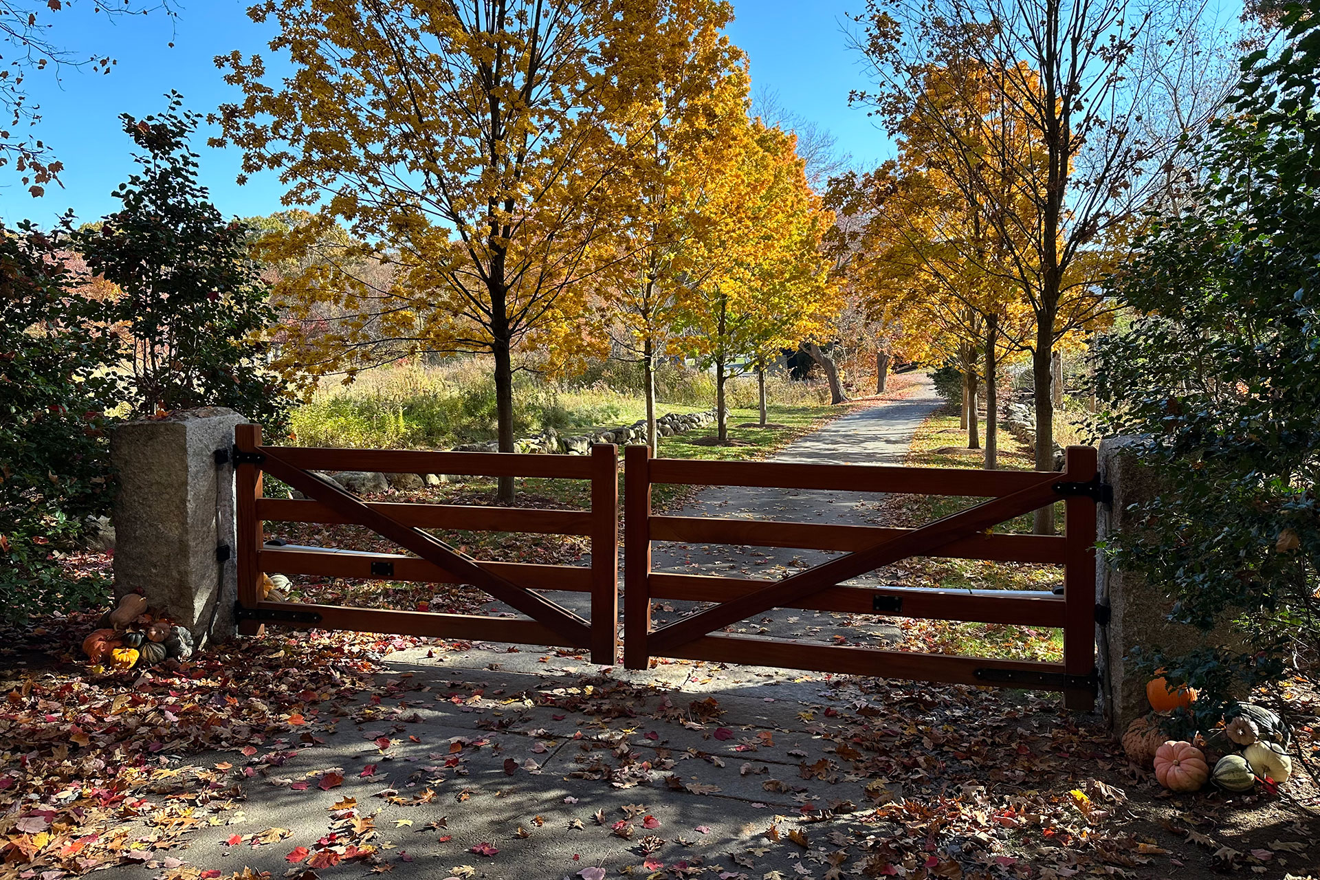 A stained wood farm gate set between granite posts gives this Concord driveway a timeless, rural character and clear boundary