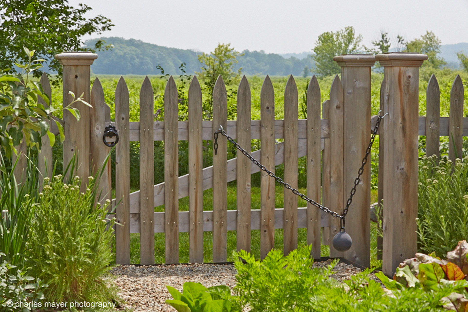 This weathered cedar gate features visible hardware that ensures smooth operation while adding handcrafted character to the garden entry.