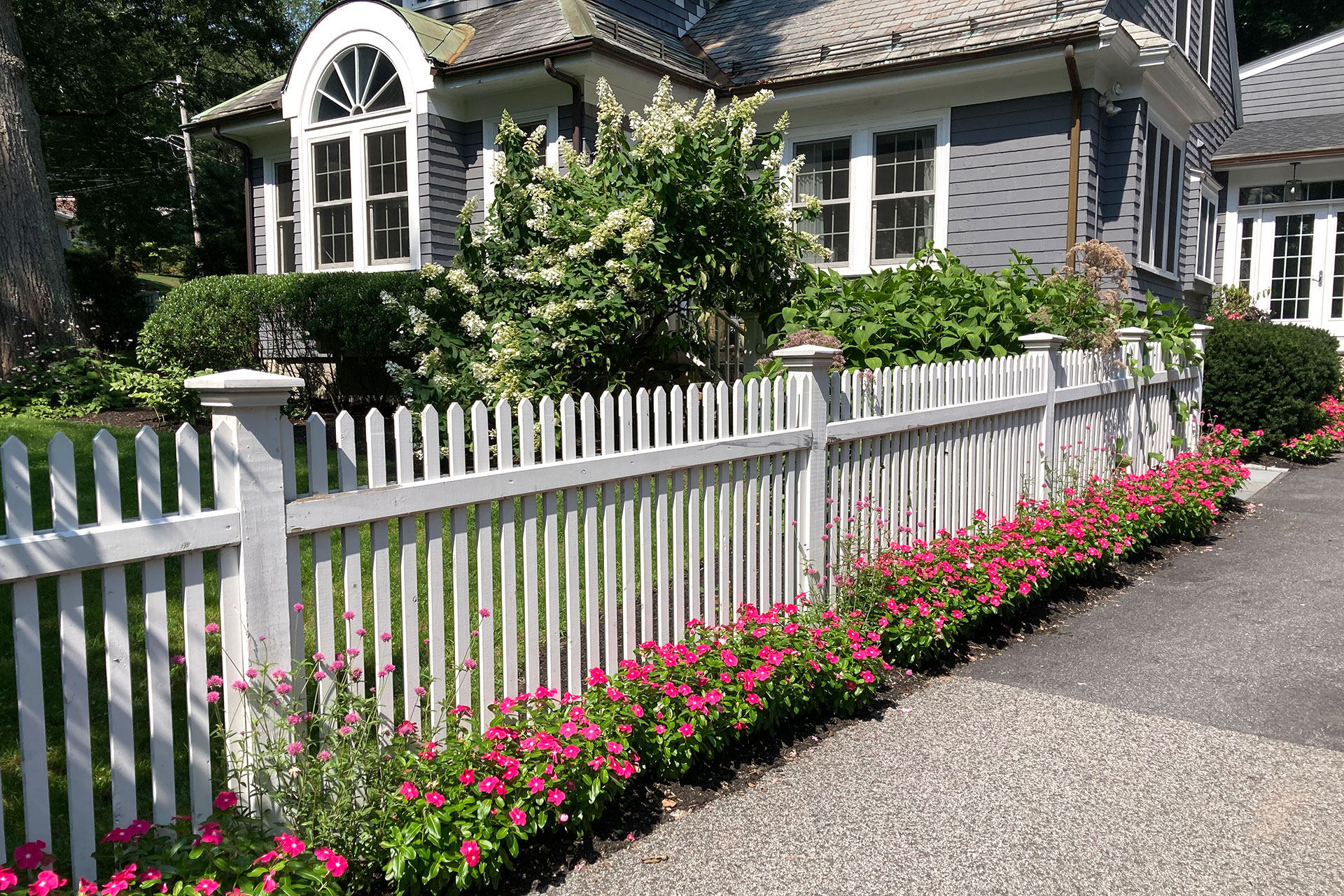 A traditional white picket fence adds timeless New England charm, gently separating front yard and street without feeling restrictive.
