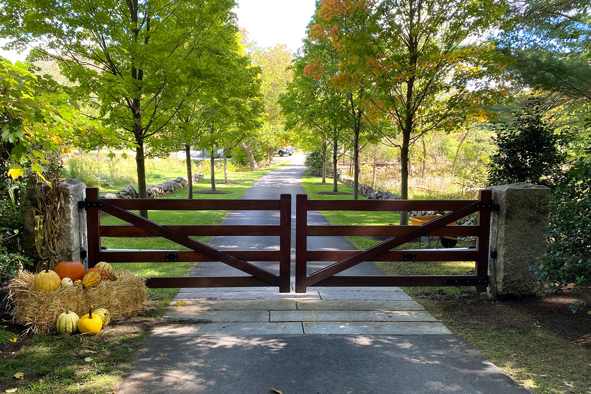 A solid wood driveway gate anchors this maple-lined entrance, adding privacy, security, and a strong sense of arrival for a Massachusetts estate.