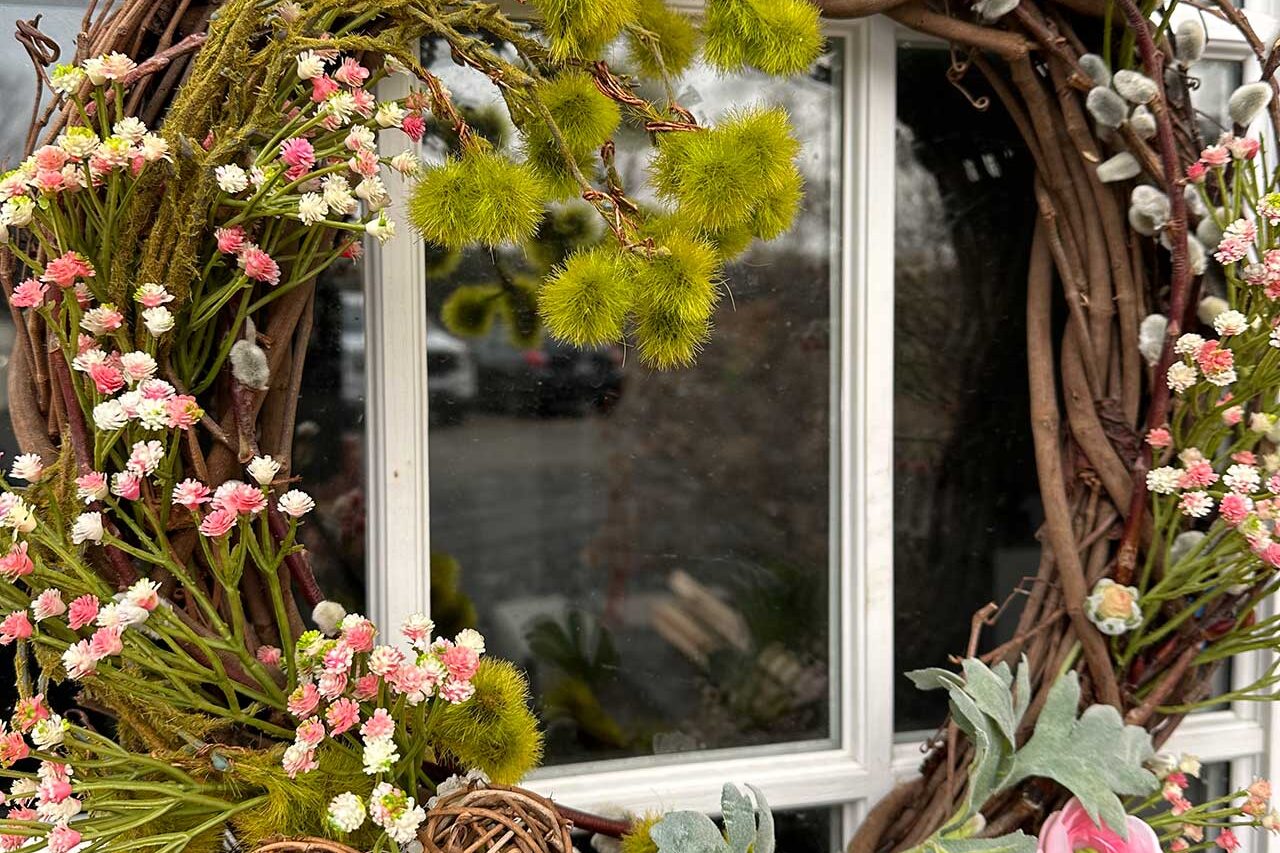 A grapevine wreath with pink blooms and soft botanical accents brings a light, garden-inspired touch to the door.