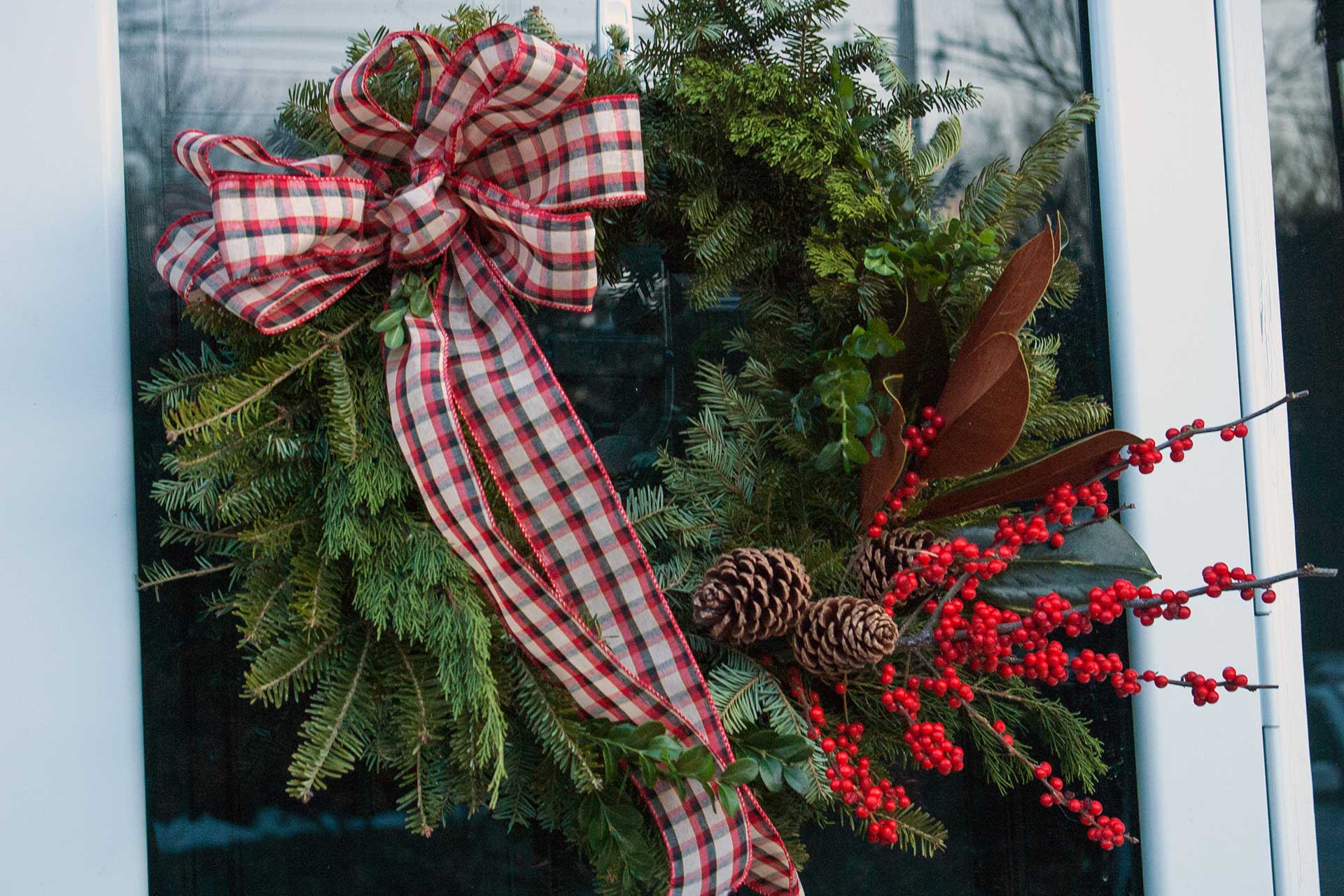 A full evergreen wreath with plaid ribbon, bright red berries, and pinecones adds classic holiday color and texture to the entry.