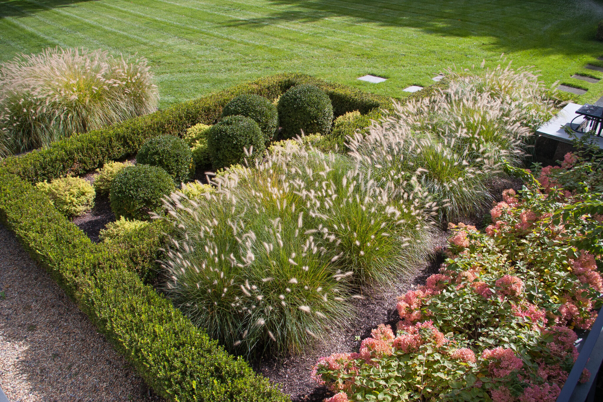 Ornamental grasses planted along the patio edge add soft texture, movement, and muted green tones, creating a relaxed coastal feel while gently framing the space without blocking views.